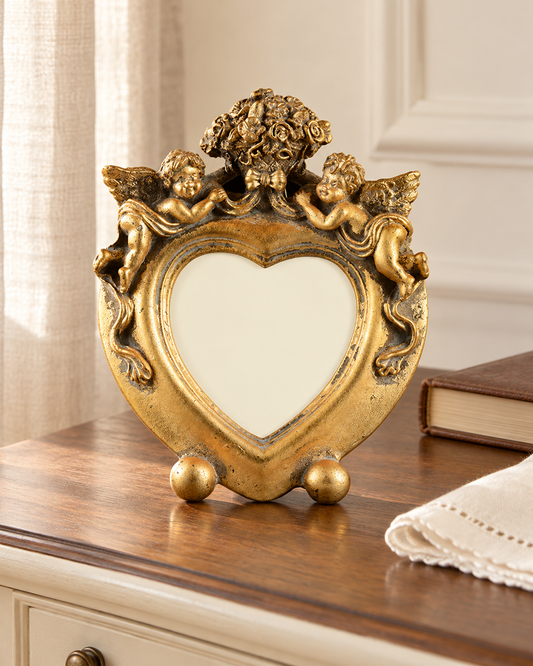 Portafoto a cuore dorato GE36523 con cherubini, ambientato su comodino chiaro.